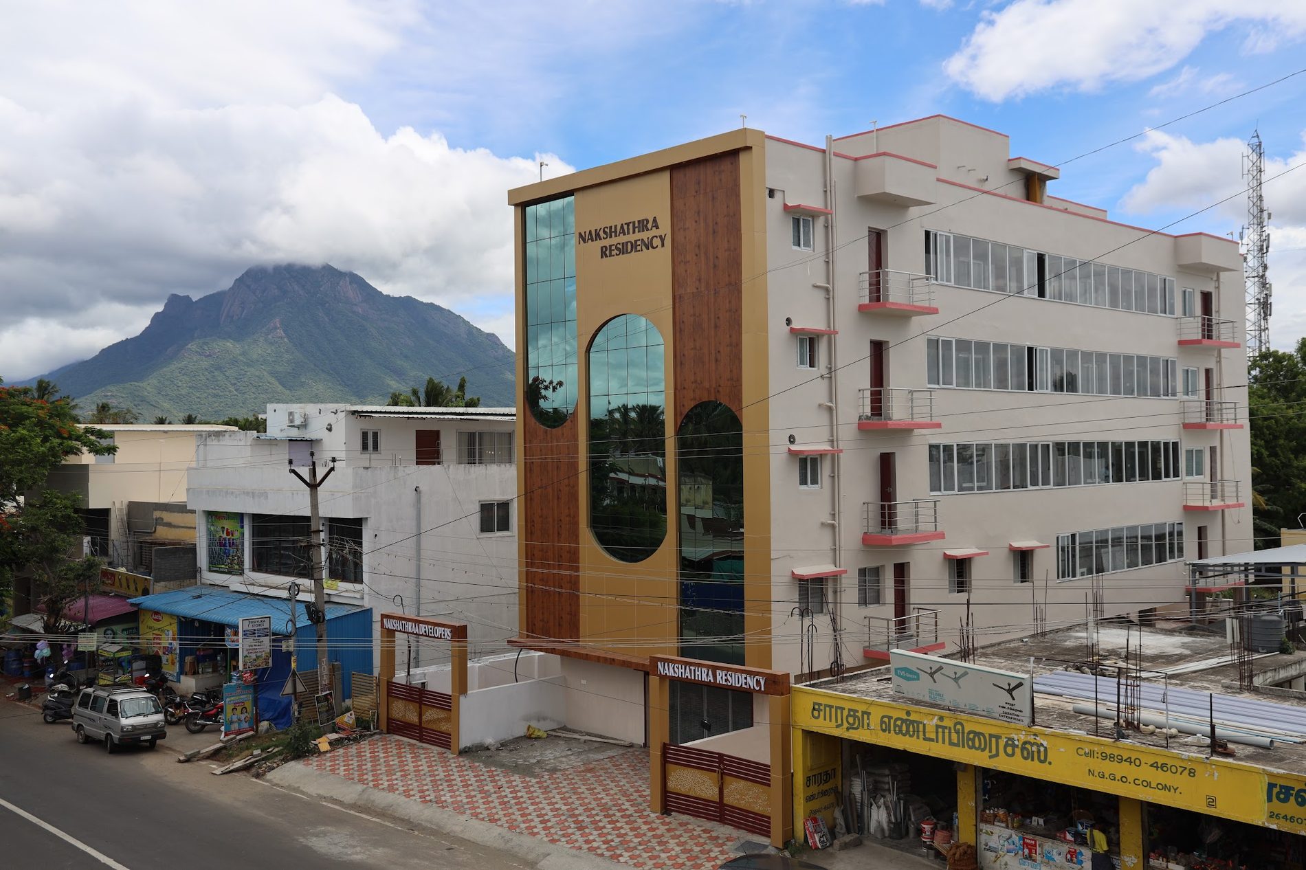 Nakshathra Residency, a five-storey building with a tall glazed entrance tower, photographed from the road with a rocky hill rising behind it.