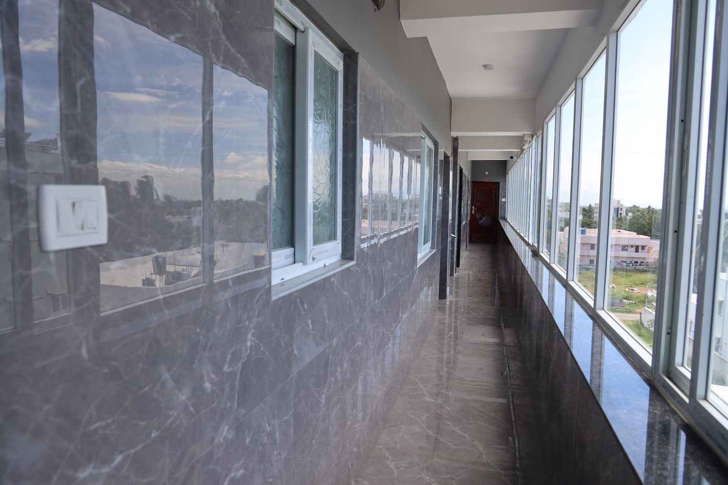 A long common corridor glazed along its full right-hand side, with marble-finish walls and floor.