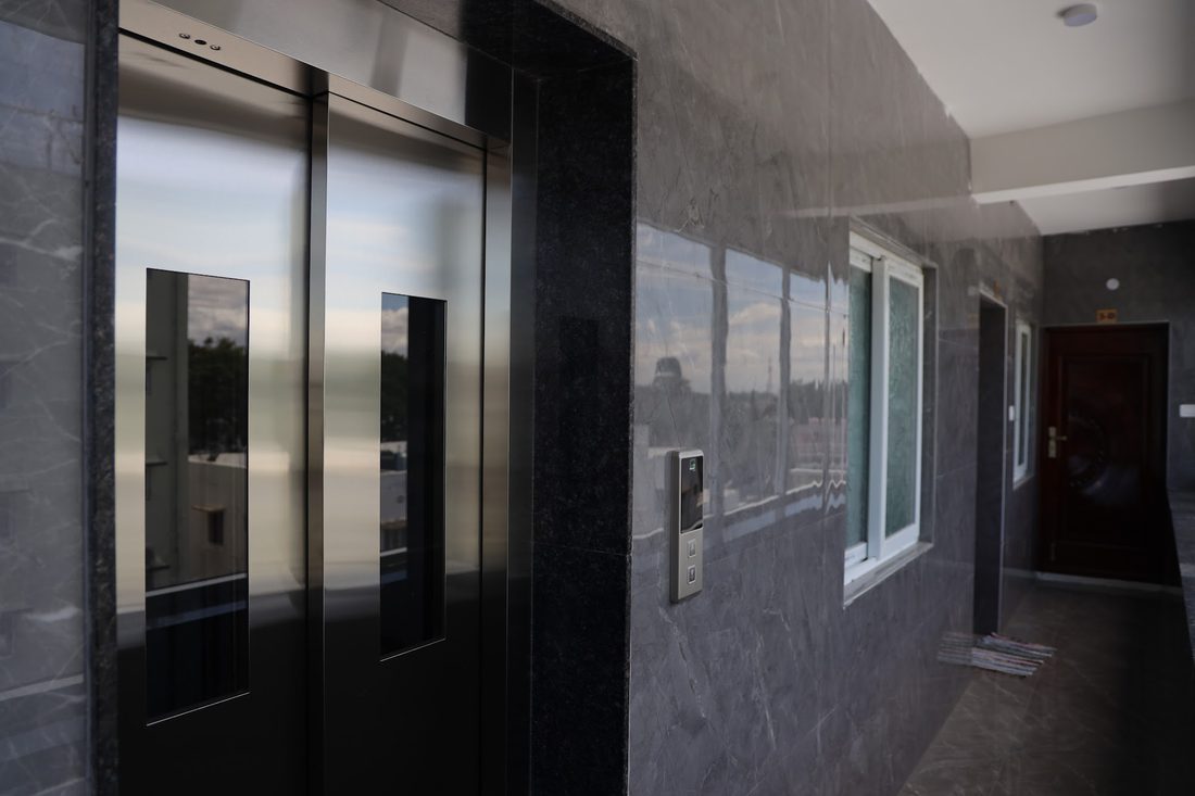The lift on an upper-floor landing, with brushed steel doors set into a dark marble surround.